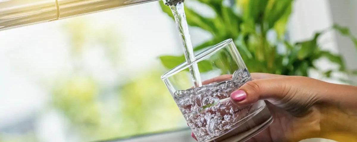 Main remplissant un verre d'eau au robinet