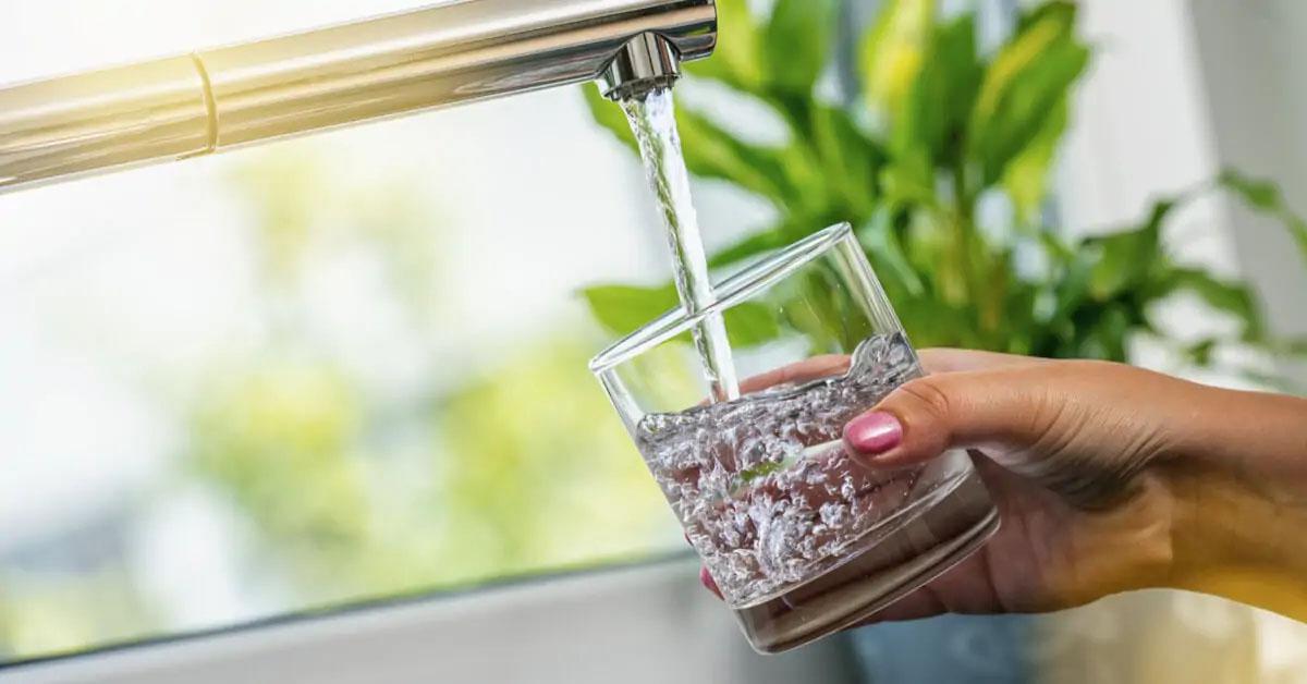 Main remplissant un verre d'eau au robinet