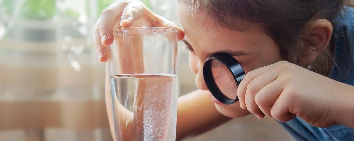 Petite fille regardant un verre d'eau à la loupe