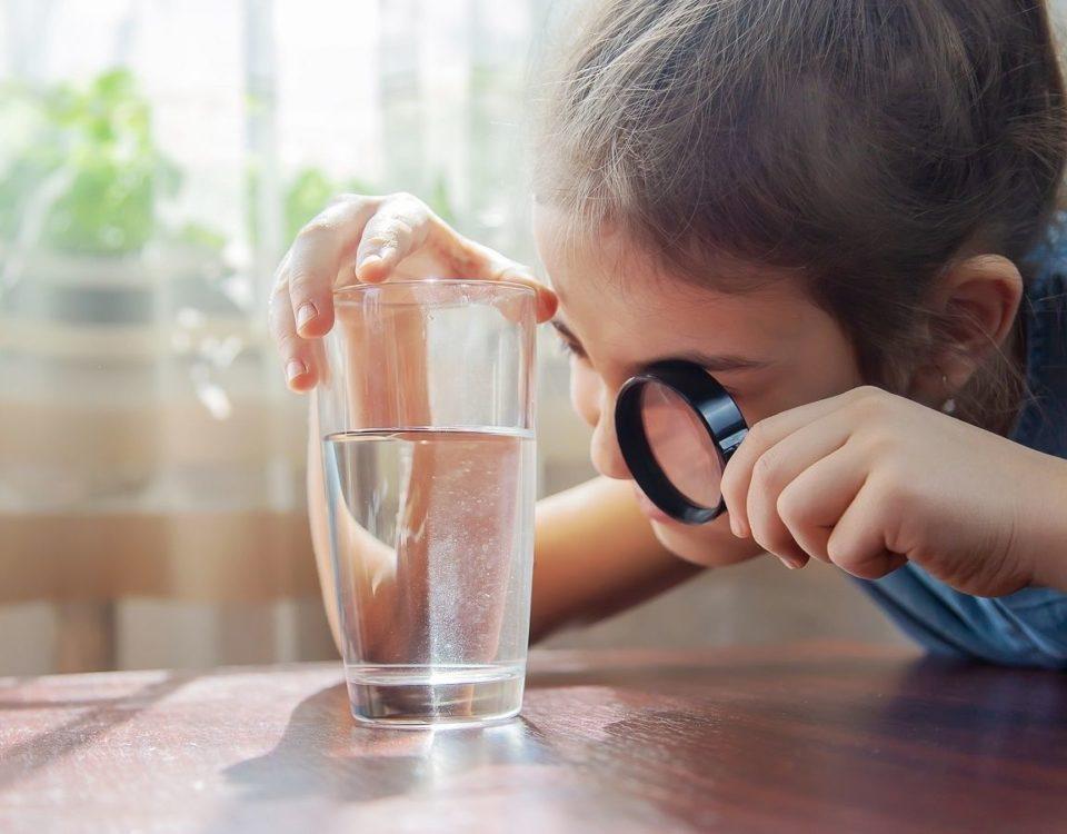 Petite fille regardant un verre d'eau à la loupe