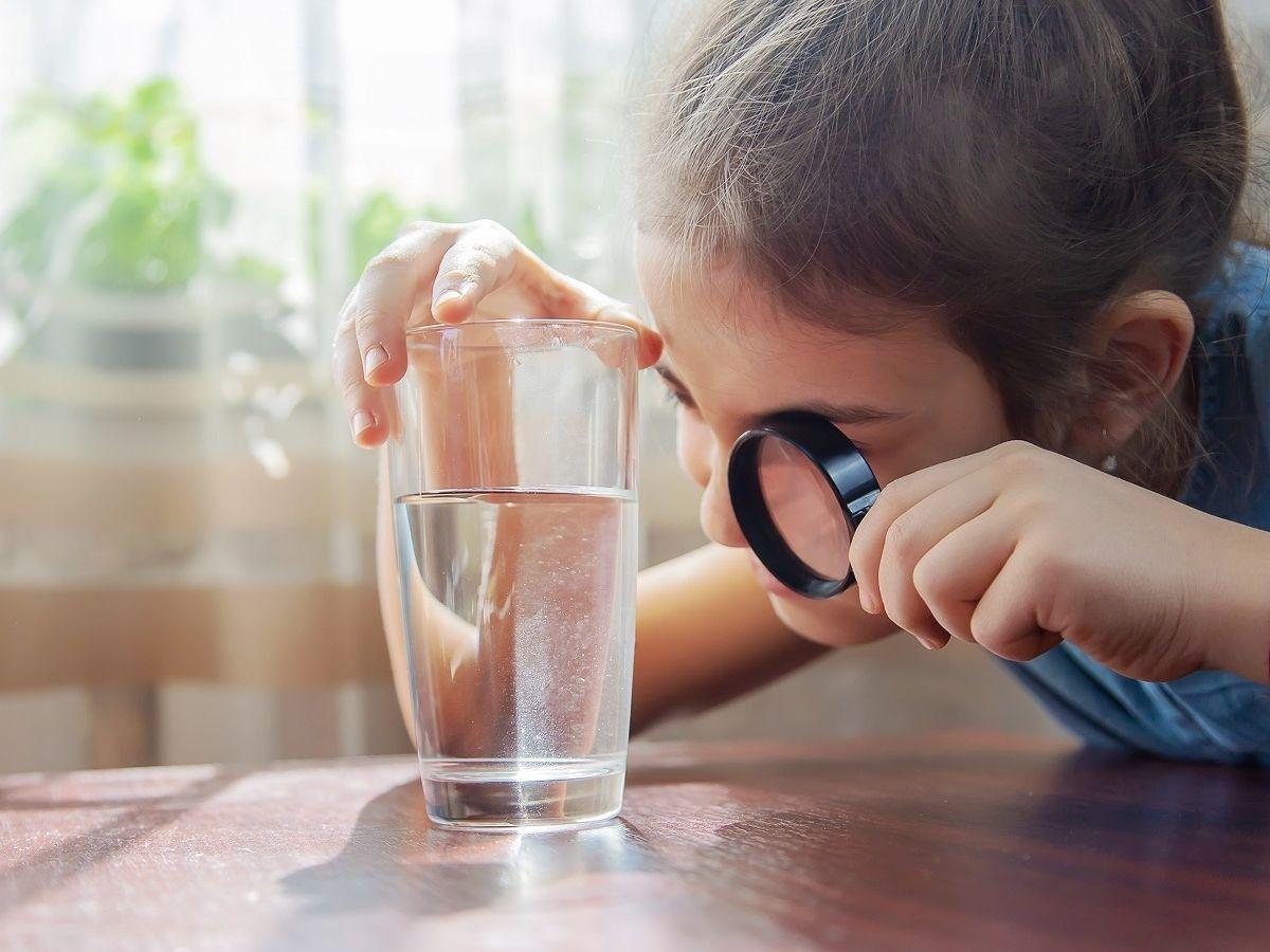 Petite fille regardant un verre d'eau à la loupe